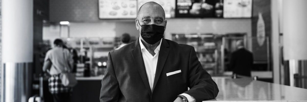 FDY, Inc President and CEO wearing a dark suit and facemask in front of one of their food franchises.